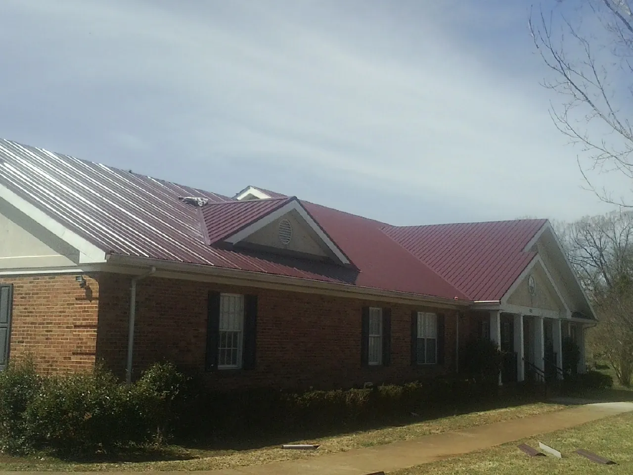 Red metal roof with gabled entries on a long brick building, from a Hail Damage Roof Repair job in Murtaugh
