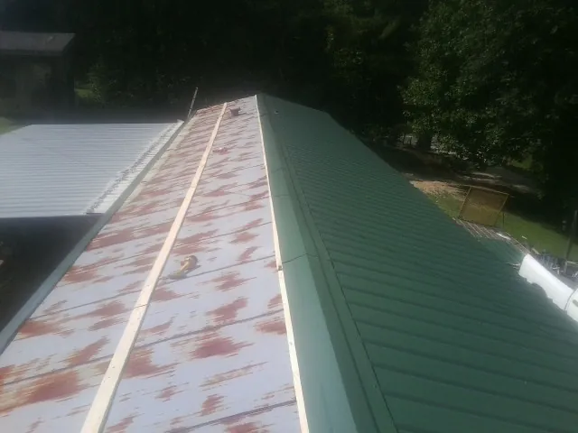 Old rusted panels beside newly installed green metal roofing — Wind Damage Roof Repair by Roofing Brothers in Murtaugh