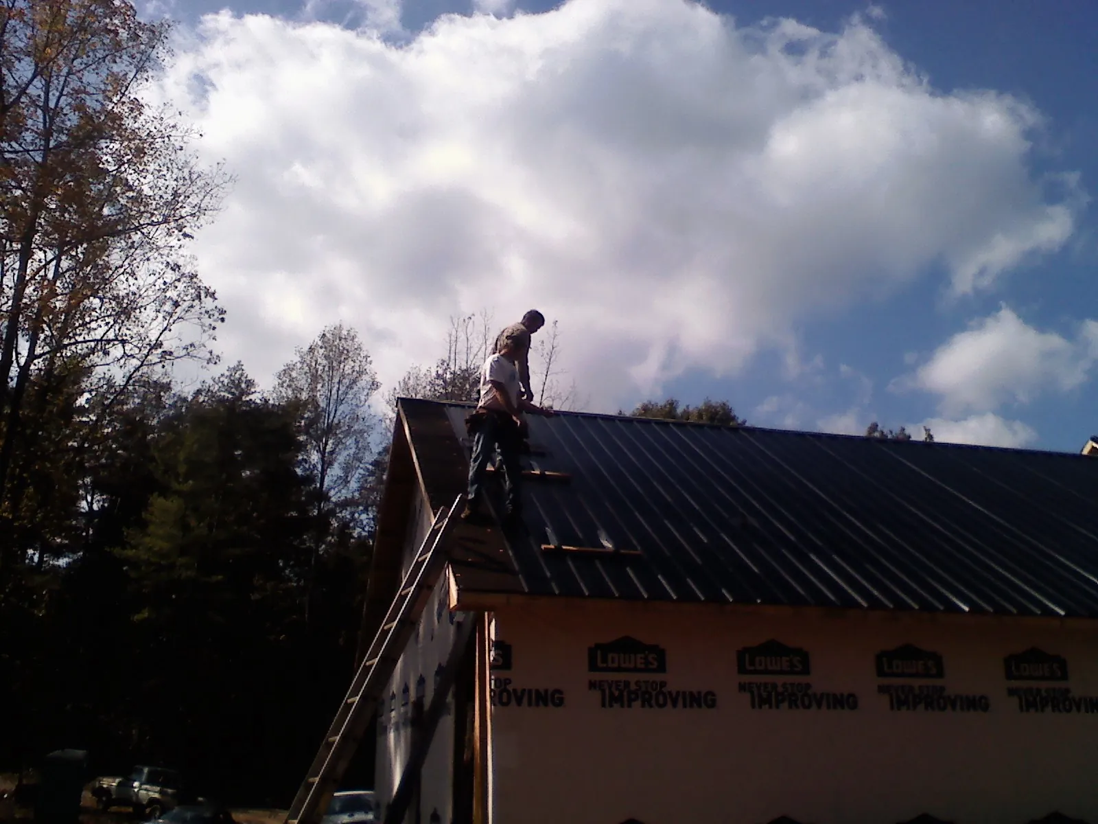 Roofer fastening dark metal panels high against a cloudy sky, from a Roof Inspection job in Murtaugh
